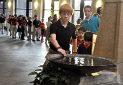 Preston Saddler, an 8th grader at St. Bartholomew School in Columbus, dips a finger into a holy water font at St. Bartholomew Church on Dec. 5, 2012, while on his way to a school Mass. In January, schools and religious education programs across the archdiocese started to use the Assessment of Catechesis and Religious Education to help learn about the knowledge and practice of students’ faith. (File photo by Sean Gallagher)