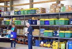 Jane Crady, coordinator of disaster preparedness and response for archdiocesan Catholic Charities, and Jim Smith stand in front of rows of supplies in the Catholic Charities Disaster Response Logistics Center in North Vernon. (Photo by Leslie Lynch)