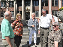 The joy of being together shows in the interaction of the organizers of the upcoming 50-year reunion involving all nine Indianapolis Catholic high schools that had graduating seniors in 1965. Steve Gutzwiller, left, Dottie Powell, Nancy Whitfield Rasmussen, Kevin Farrell and Carolyn Perrin McMahon share a laugh on the steps of the old Cathedral High School, now the Archbishop Edward T. O’Meara Catholic Center in Indianapolis. (Photo by John Shaughnessy)