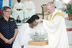 Father Christopher Wadelton, pastor of St. Philip Neri Parish in Indianapolis, baptizes Holy Cross Central School student Jada Brown during a school Mass in the chapel space for Holy Cross School in Indianapolis on April 20. Also pictured at left is Ruth Hittel, principal of the school. (Photo by John Shaughnessy)