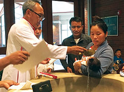 Bishop Lucius Hre Kung of the Diocese of Hakah in Myanmar, left, baptizes Bernadette Ngun, the child of two Myanmar refugees, on July 7 during the bishop’s visit to St. Barnabas Parish in Indianapolis. Ngun is held by her mother Monica Shwe, while family friend Robert Hram Hei looks on. (Photo by Patty Cain)