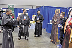 Conventual Franciscan Brother Joseph Martin Huang takes a photo of a National Catholic Youth Conference participant from the Covington, Ky., Diocese standing beside life-size cutouts of St. Francis of Assisi and St. Thérèse of Lisieux on Nov. 16 in the conference’s Thematic Village in the Indiana Convention Center in Indianapolis. Looking on are Conventual Franciscan Fathers John Bamman, second from left, and Jijo Thomas. (Photo by Sean Gallagher)