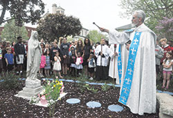 With students of St. Joan of Arc School looking on, Father Guy Roberts, pastor of St. Joan of Arc Parish in Indianapolis, blesses on May 3 a newly created rosary garden on the parish’s grounds. The school’s seventh- and eighth-grade classes created the garden through a grant from Queen and Divine Mercy Center Endowment Fund, managed by the archdiocesan Catholic Community Foundation. (Photo by Sean Gallagher)