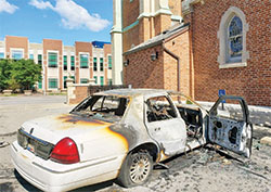A burned car sits on May 30 in the parking lot of St. John the Evangelist Parish in Indianapolis, set on fire by an arsonist the night before in violence amid protests related to the death of George Floyd. (Submitted photos)