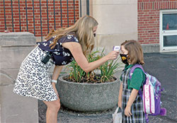 Assistant principal Kortney Wenclewicz checks the temperature of first-grade pupil Maddy Weber on Aug. 20, the first day of classes at Christ the King School in Indianapolis. (Photo by John Shaughnessy)