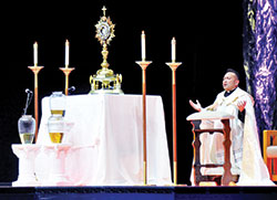 Voluntas Dei Father Leo Patalinghug kneels in worship during an evening of eucharistic adoration in Lucas Oil Stadium in Indianapolis on Nov. 19, 2021, during the National Catholic Youth Conference. (File photo by Natalie Hoefer)