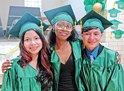After their graduation ceremony at Holy Cross Central School in Indianapolis on May 24, Ashley Aguilar Perez, left, Ashaundi Copeland and Elkin “Santiago” Vera Lamprea share a moment of togetherness. (Photo by John Shaughnessy)
