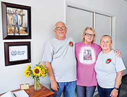 Tony Talbert, left, and his wife Donna Talbert, right, pose with Vicky Greer, the mother of David Marshal for whom the new David’s House St. Vincent de Paul ministry in Richmond was named. Marshall’s photo is seen hanging on the wall. (Photo by Natalie Hoefer)