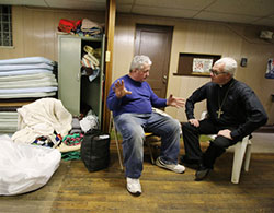 Bishop Donald J. Hying listens to Geg Garner, one of the men staying at the Men's Homeless Shelter Saturday Feb. 20. Bishop Hying visited the shelter, located in the basement of Michigan City's Sacred Heart Church, looking to be a conduit for assistance to help the shelter. A stack of mats and a closet of blankets will be laid out to provide bedding for the men. (Bob Wellinski photo)