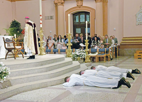 Transitional deacons Thomas Day, left, Liam Hosty and Isaac Siefker lay prostrate in prayer on June 7 in SS. Peter and Paul Cathedral during the Mass in which they were ordained as priests. Joining them in prayer is Archbishop Charles C. Thompson. (Photos by Sean Gallagher) 