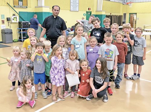 Father Jegan Peter, pastor of St. Vincent de Paul Parish in Bedford and St. Mary Parish in Mitchell, poses in St. Vincent de Paul’s school gym with some of the children involved in the two faith communities’ Family of Faith catechetical program. (Submitted photo)
