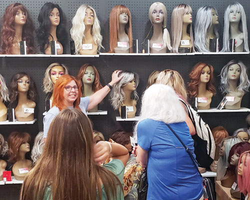 Bonnie Wentworth talks with customers about the upscale wigs she sells in Penelope’s Covered Blessings shop in Madison on July 11. A portion of the proceeds from all items sold in the shop, including faith-based merchandise—both Catholic-specific and general Christian—go toward helping patients at Norton Cancer Institute in Madison and those suffering hair loss from cancer and other medical conditions. (Photo by Natalie Hoefer)