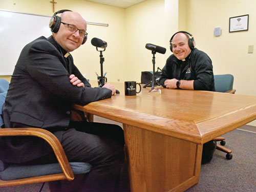 Father Michael Keucher, left, and Father Adam Ahern pose on Feb. 10 at the Archbishop Edward T. O&rsquo;Meara Catholic Center in Indianapolis with equipment they use in producing the first season of their podcast &ldquo;Priest Cast,&rdquo; which they posted on a daily basis from Holy Thursday last year through Holy Thursday earlier this month. (Photo by Sean Gallagher)