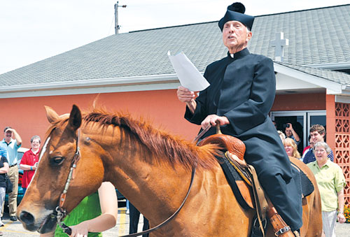 Father Paul Landwerlen, administrator at the time of St. Vincent de Paul Parish in Shelby County, reads a proclamation about the faith community’s 175-year history after riding a horse onto its grounds on June 24, 2012. St. Vincent’s founding pastor Father Vincent Bacquelin rode on horseback to minister to Catholics throughout central and eastern Indiana. (Criterion file photo)