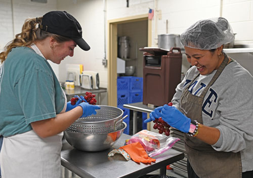 Therese Hauersperger, left, a member of the college student organization of St. John the Evangelist Parish in Indianapolis, and Leslie Venegas, a Fellowship of Christian University Students’ missionary at the parish, prepare food on Oct. 9 for the Cathedral Kitchen in Indianapolis. On Nov. 8, an open house and blessing will highlight recent Cathedral Kitchen restorations, including upgrades to electrical, plumbing and structural systems. (Photo by Emily Mastronicola)