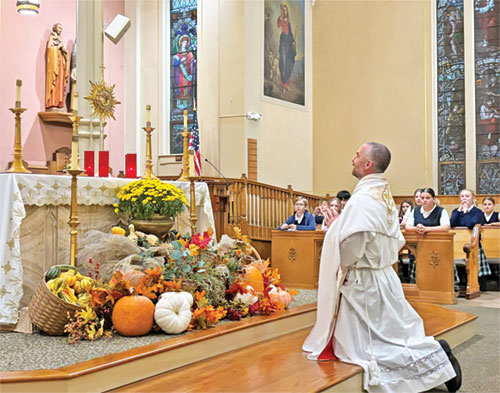 Father Dustin Boehm and students at St. Gabriel School in Connersville kneel during eucharistic adoration on Oct. 7 in St. Gabriel Church. (Photo by Mary King)