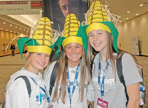Vivian McCombs, left, Frankie Gotto and Addison Allaman of St. John Vianney Parish in Bettendorf, Iowa, in the Diocese of Davenport, show their state pride by wearing corn-in-the-husk headgear during the National Catholic Youth Conference in Indianapolis on Nov. 20-22. (Photo by John Shaughnessy)