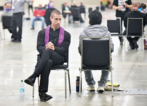 Father Isaac Siefker hears a confession on Nov. 21 in an exhibit hall at the Indiana Convention Center in Indianapolis used for the sacrament of penance during the National Catholic Youth Conference. The priest is parochial vicar of Holy Name of Jesus Parish in Beech Grove and Good Shepherd in Indianapolis. (Photo by Sean Gallagher)