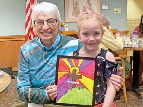 Benedictine Sister Mary Luke Jones of Our Lady of Grace Monastery in Beech Grove shares a smile with Margo Pierle, a kindergarten student at Christ the King School in Indianapolis. Margo holds a framed artwork she created that helped raise $1,547 that the kindergarten students donated to the sisters at the monastery. (Photo by John Shaughnessy)
