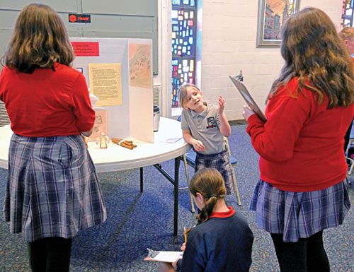 Standing at center, Eisley Smith, a second-grade student at Sacred Heart School in Jeffersonville, explains the Second Station of the Eucharist to other students in the parish&rsquo;s activity center on March 12 during a Stations of the Eucharist exhibit she and her classmates created and presented as part of a project preparing them to receive their first Communion. (Photo by Natalie Hoefer)