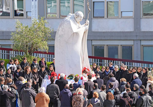 Young people and members of the House of Mary, groups associated with the Pontifical Academy of the Immaculate Conception, and others pray around a statue of St. John Paul II outside Rome’s Gemelli hospital March 2, 2025. Pope Francis is receiving treatment there for double pneumonia. (CNS photo/Lola Gomez)
