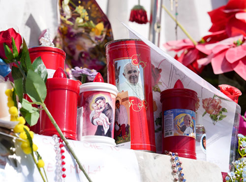 Votive candles and flowers are seen at the base of a statue of St. John Paul II outside Rome's Gemelli hospital March 6, 2025, where Pope Francis has been hospitalized since Feb. 14, receiving treatment for double pneumonia. (CNS photo/Lola Gomez)