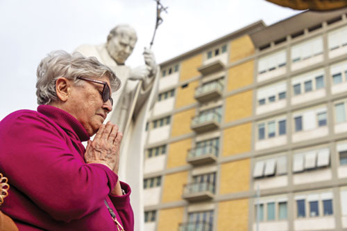 A woman prays near a statue of St. John Paul II outside Rome's Gemelli hospital where Pope Francis is receiving treatment March 8, 2025. (CNS photo/Pablo Esparza)