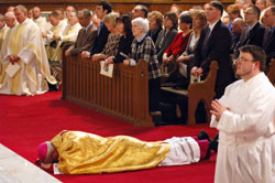 Bishop Christopher J. Coyne, the new auxiliary bishop of the Archdiocese of Indianapolis, lays prostrate in prayer on March 2 before the altar and sanctuary at St. John the Evangelist Church in Indianapolis during the praying of the Litany of the Saints as part of his episcopal ordination Mass. His mother, Rita Coyne of Woburn, Mass., center, and other members of his family kneel in prayer in the pews behind him. Bishop Coyne’s posture is a prayerful sign of humility before God and obedience to the ministry that he has been called by Pope Benedict XVI to serve the Catholic Church in central and southern Indiana. Seminarian Jerry Byrd, a member of St. Louis Parish in Batesville, is shown to the right of Bishop Coyne. (Photo by Sean Gallagher)