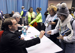 Bishop Charles C. Thompson of Evansville, Ind., left, gives a signed trading card of himself to Catherine Nguyen of New Orleans on Nov. 18 in the National Catholic Youth Conference’s thematic park at the Indiana Convention Center in Indianapolis. (Photo by Sean Gallagher)