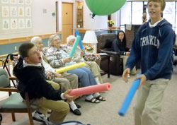 During a visit to the Franklin United Methodist Community, St. Rose of Lima students Nate Fries, left, and Ethan Sullivan bring smiles to senior citizens as they use large, foam sticks to bounce balloons around the activity room. (Submitted photo)