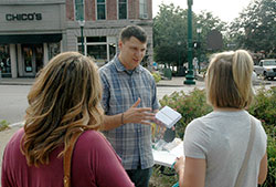 Steve Dawson believes two-minute conversations with strangers about his Catholic faith can lead them closer to God. Here, the founder of St. Paul Street Evangelization talks about the difference Christ has made in his life with two women on a street corner in Bloomington on Aug. 4. (Photo by John Shaughnessy)
