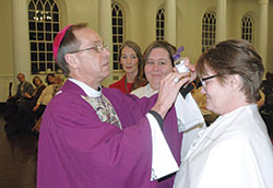 As part of administering the sacrament of confirmation, Archbishop Charles C. Thompson prepares to make the sign of the cross with sacred chrism oil on the forehead of Marguerite Engle during a Mass at the Indiana Women’s Prison chapel in Indianapolis on the evening of March 4. Engle and Opal Williams, third from left, received the sacraments of baptism, confirmation and the Eucharist during the Mass. In the background, Andrea Wolsifer of St. Anthony Parish in Indianapolis watches the two women whom she guided through the Rite of Christian Initiation of Adults to be received into the full communion of the Church. (Photo by John Shaughnessy)