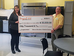 Development director Dawn Bennett and agency director Mark Casper, both of St. Elizabeth Catholic Charities in New Albany, hold a symbolic check representing $50,000 that the organization won last September through Impact 100 of Southern Indiana’s inaugural annual grant. The money was used to build a multiple-station kitchen to implement a new residential culinary training program, and to renovate a shelter kitchen for both training practice and residential use. Bennett and Casper are standing in the renovated kitchen. (Submitted photo)