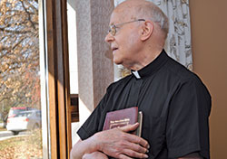 In this photo from Nov. 27, 2013, retired Father Herman Lutz, gazes out of the main parlor window of St. Paul Hermitage in Beech Grove, the retirement home where he and three other retired archdiocesan priests reside. (Photo courtesy of the archdiocesan Office of Stewardship and Development)