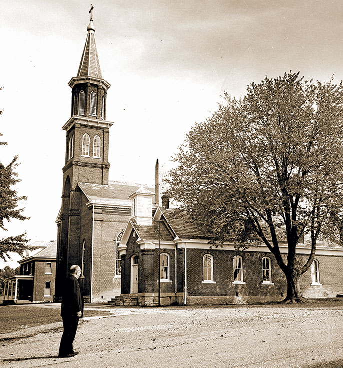 In this photo from 1966, Father Robert Wilhelm is seen near St. Ann Church in Jennings County. The parish was founded in 1841. The brick church building, still in use, was constructed in 1866 and succeeded an original log structure. Father Wilhelm was the pastor of St. Ann Parish, as well as the former St. Denis Parish in Jennings County, from 1957-67. 