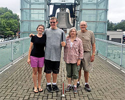 Amanda Noles, her son Cayden, and her parents, Don and Linda Dale, pose for a photo with the World Peace Bell in Newport, Ky., in the background. Cayden, who is blind and autistic, loves the ringing of bell systems, so as a surprise for his 16th birthday his mother planned a weeklong journey to visit bell systems in Kentucky and Indiana, including one of his favorites at St. Michael Church in Cannelton in southern Indiana. (Submitted photo)