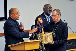 Archbishop Charles C. Thompson holds a basket containing written accounts of experiences of racism being blessed by Bishop Shelton J. Fabre, chairman of the U.S. bishops’ Ad Hoc Committee against Racism, during a listening session on racism held at Marian University in Indianapolis on Sept. 30. Fifteen Catholics from across central and southern Indiana told the stories of their experiences of racism at the event that drew approximately 100 attendees. Holy Cross Brother Roy Smith, center, served as master of ceremonies for the session. (Photo by Sean Gallagher)
