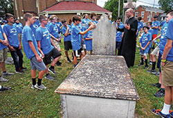 In the cemetery of St. Vincent de Paul Parish in Shelby County on July 10, archdiocesan vocations director Father Michael Keucher gathers with Bishop Bruté Days participants around the grave of Father Vincent Bacquelin, the first priest to minister regularly in central Indiana. (Photo by Sean Gallagher) 