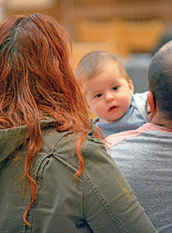Ethan Moncayo peeks between the heads of his parents Karina Ramirez and Marco Moncayo, members of St. Patrick Parish in Indianapolis, during the Respect Life Mass at SS. Peter and Paul Cathedral in Indianapolis on Oct. 4. (Photo by Natalie Hoefer)