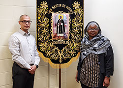 Amid the devastating impact of COVID-19, Oscar Castellanos and Pearlette Springer have adapted their approaches to deepen the faith lives of Hispanics and Blacks across the archdiocese. Castellanos is director of Intercultural Ministries for the archdiocese while Springer is the coordinator of Black Catholic Ministry. They are pictured with a banner of St. Martin de Porres. Their communities have a shared love for the saint, who was the son of a Spanish nobleman and a freed Panamanian slave of African descent. (Photo by Brandon A. Evans)