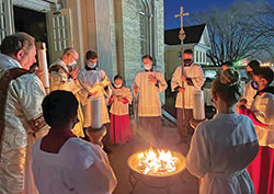 Altar servers and Deacon Thomas Hill, left, surround a fire outside of St. Joseph Church in Shelbyville on April 3 while Father Michael Keucher, St. Joseph Parish’s pastor, prays at the start of the faith community’s Easter Vigil. (Submitted photo)