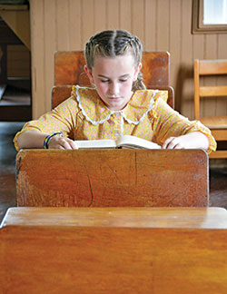 Lillian Koeppel, a 9-year-old member of St. Mary Parish in Navilleton, sits in an old-fashioned school desk in the schoolhouse the parish built in 1893 that now serves as a museum. (Photo by Natalie Hoefer)