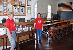 Angie Atkins, left, and Anna Sweeney stand in the one-room Navilleton schoolhouse they attended and later helped restore as a museum. It was built by their parish, St. Mary, in 1893. (Photo by Natalie Hoefer)