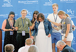 Marian University students who are part of the school’s San Damiano Scholarship program pray with Shannon Wimp Schmidt before she gives a keynote address on Aug. 13 at Marian during the archdiocesan-sponsored Into the Heart Conference for people from many backgrounds involved in the lives of youths. (Submitted photo)