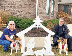St. Malachy Parish in Brownsburg is one of the 28 schools and parishes in central Indiana that participated in the continuing effort to emphasize the true meaning of Christmas and help make central Indiana the “Outdoor Nativity Scene Capital of the United States,” the goal of Jim Liston, who started the program. Jean McCorkhill, St. Malachy’s coordinator of children’s faith formation, and Father Sean Danda, pastor of the parish, pose by one of the Nativity scenes with Father Danda’s dogs, Finley and Bentley. (Submitted photo)