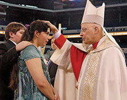 Cardinal Francis E. George of Chicago confirms Alisha Webber, a member of Holy Family Parish in Oldenburg, during a May 3, 2009, Mass at Lucas Oil Stadium in Indianapolis that celebrated the 175th anniversary of the founding of the Diocese of Vincennes, Ind., which later became the Archdiocese of Indianapolis. (Criterion file photo by Sean Gallagher)