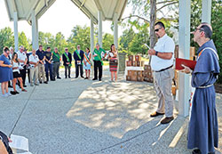 Ben Wissel, a member of the New Albany Knights of Columbus #1221 Council, second from right, recites a poem during a burial service for miscarried babies—whose tiny caskets seen in the background were built by the Knights—at Holy Trinity Cemetery in New Albany on July 14. The service was led by Conventual Franciscan Father Mark Weaver, pastor of St. Mary Parish in New Albany, at right. (Photo by Natalie Hoefer)
