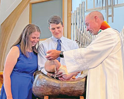 Father Christopher  Wadelton, pastor of St. Bartholomew Parish in Columbus, baptizes Charlie Bode as his smiling parents, Katie and Tom Bode, savor the celebration of the sacrament. Katie Bode and Father Wadelton are cousins who shared some time together in Portland, Ore., one of the places the priest visited this summer. (Submitted photo)