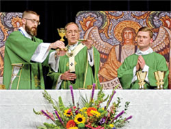 Transitional Deacon Bobby Vogel of the Archdiocese of Indianapolis, left, and Archbishop Charles C. Thompson elevate the Eucharist as archdiocesan transitional Deacon Samuel Rosko looks on during a Mass for National Catholic Youth Conference (NCYC) participants from the Archdiocese of Indianapolis in the Indiana Convention Center in Indianapolis at the opening of NCYC on Nov. 16. (Photo by Natalie Hoefer)