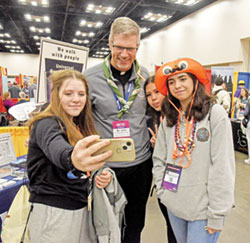 Viatorian Brother John Eustice poses for a selfie with Amanda Mullin, left, Bella Vazquez and Kara Hartz on Nov. 16 in the Indiana Convention Center in Indianapolis during the National Catholic Youth Conference. The youths came to the conference in Indianapolis from the Archdiocese of Las Vegas. Brother John, a transitional deacon, serves at Maternity of the Blessed Virgin Mary Parish in Bourbonais, Ill. (Photo by Sean Gallagher)